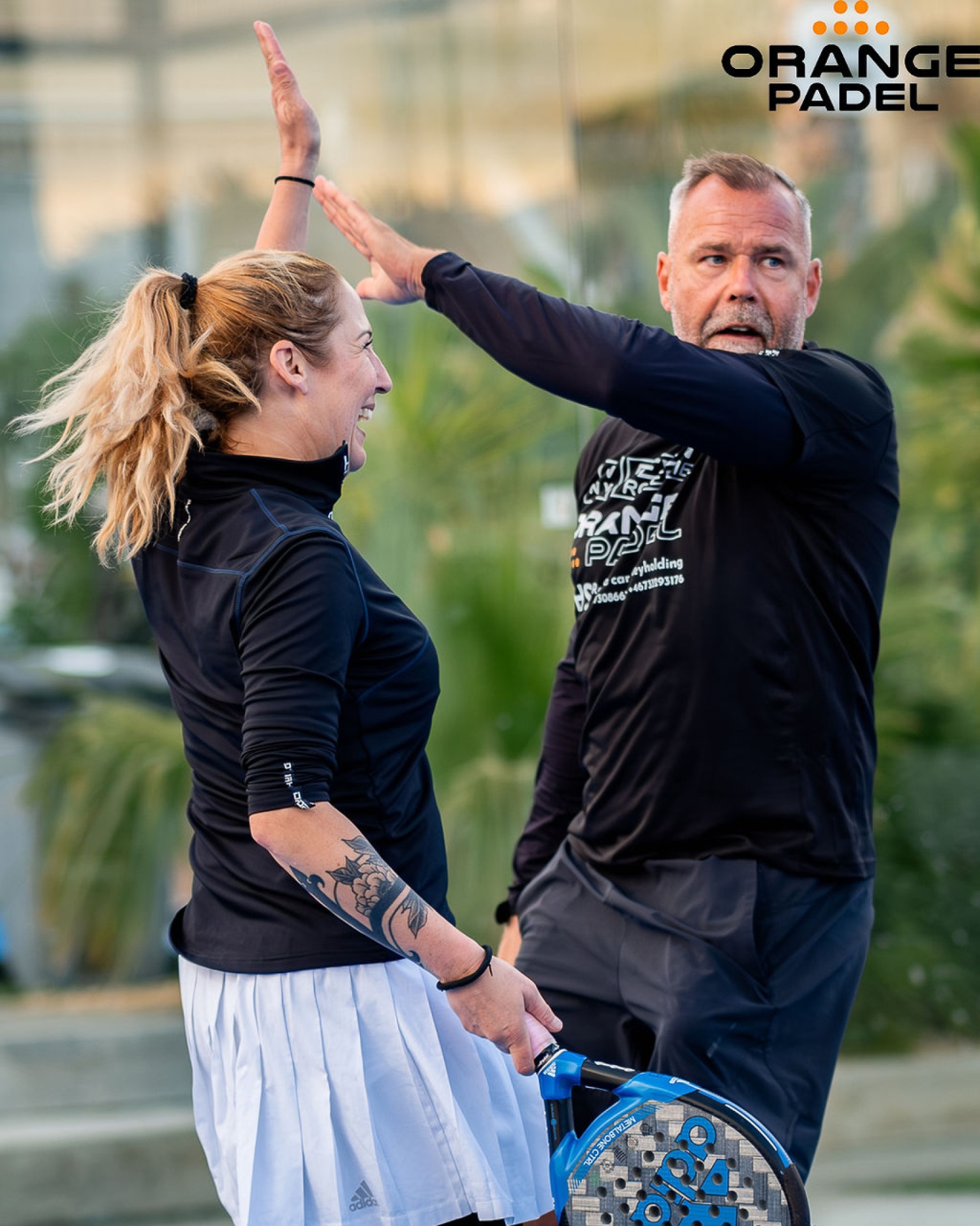 Padelspelare firar med high-five på Orange Padel-banan